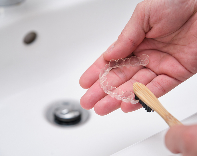 Close up of a Vivera™ retainer being cleaned with a plain wooden toothbrush