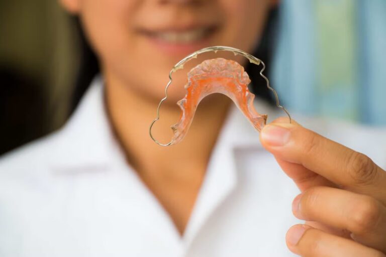 Close up of an orthodontist in her white coat holding a metal removable retainer