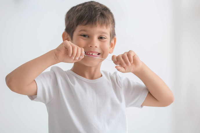 Smiling child in a white tee with dental floss wound around his index fingers