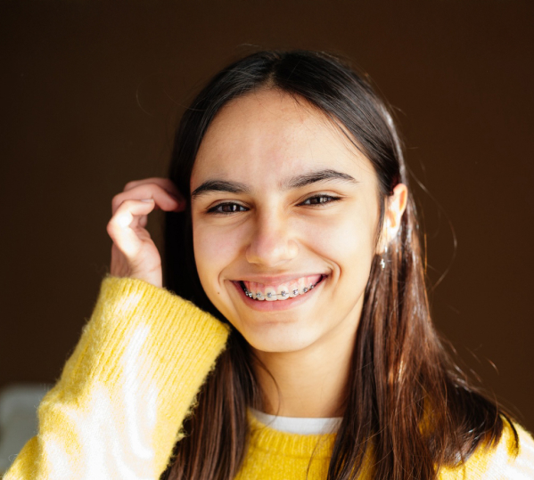 Teen with braces smiling and tucking her hair behind her ear in the afternoon sun