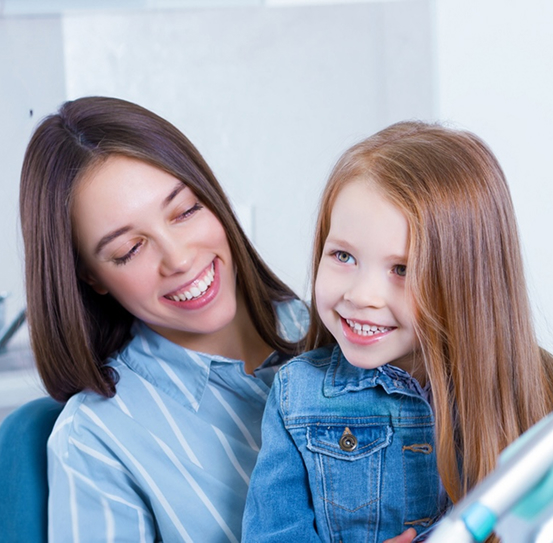 Smiling child at her early orthodontics appointment in her mother’s lap