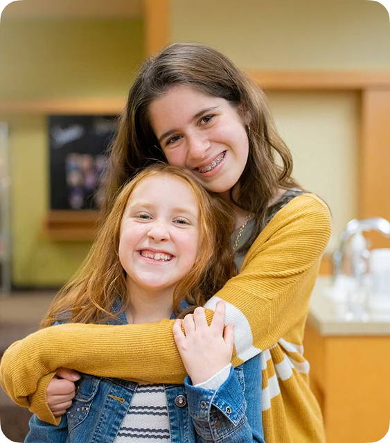 Two girls receiving orthodontic treatment at Joy of Orthodontics smiling and hugging