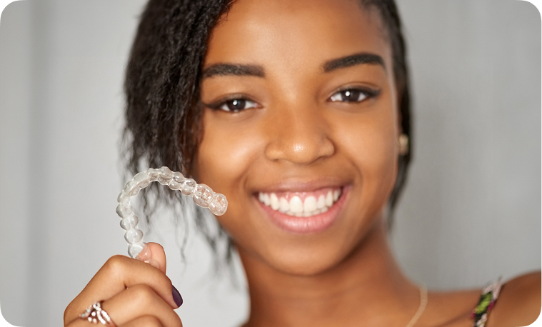 Teen with Invisalign® for teens smiling and holding her aligner