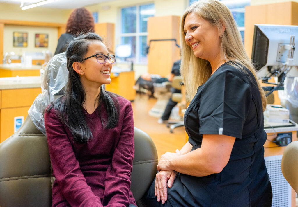 Teen Joy of Orthodontics patient smiling at her orthodontic technician after receiving orthodontic treatment