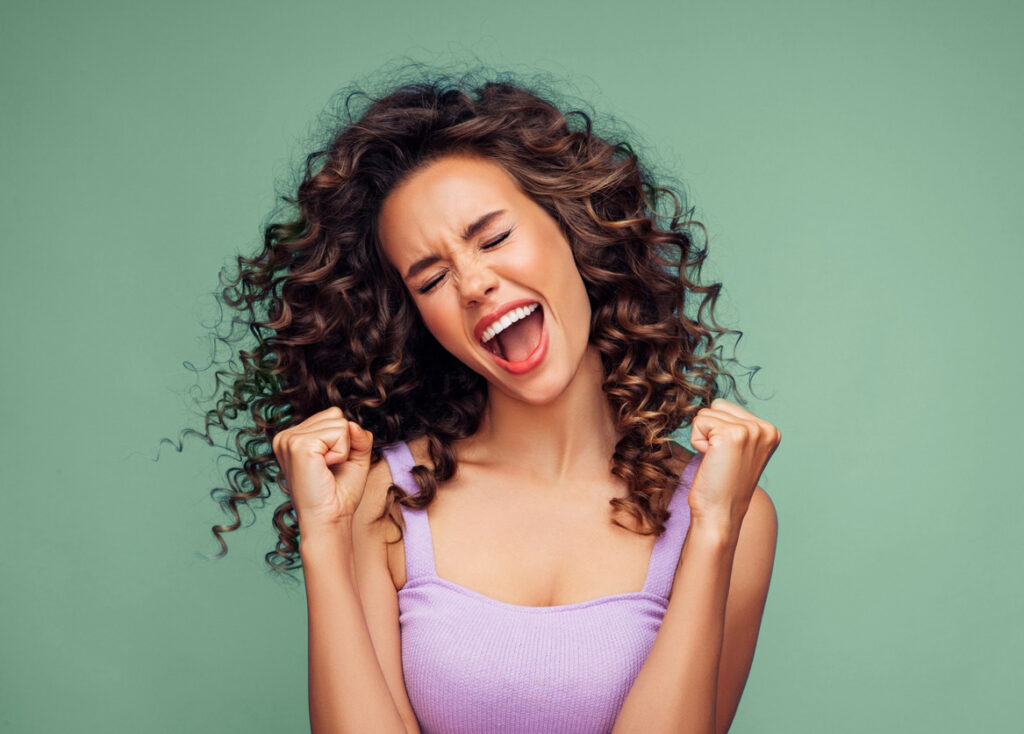 Woman with flowing curly hair doing a celebratory shout with fists clenched