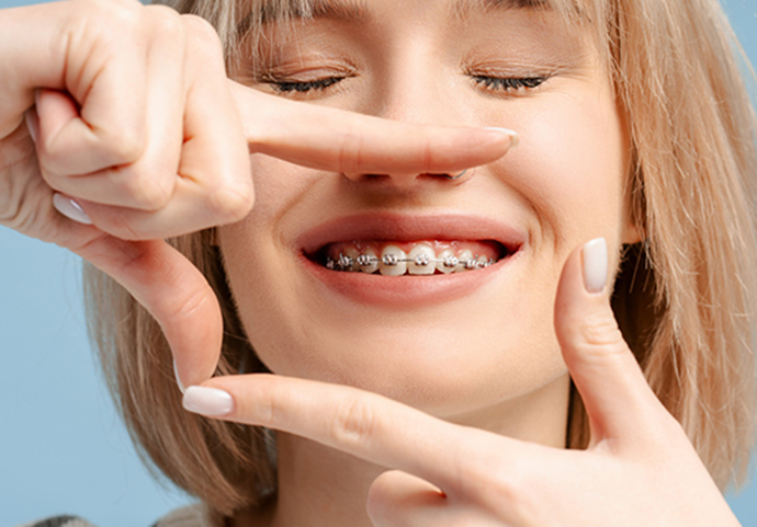 Close up of a young woman with braces smiling framing her smile with fingers