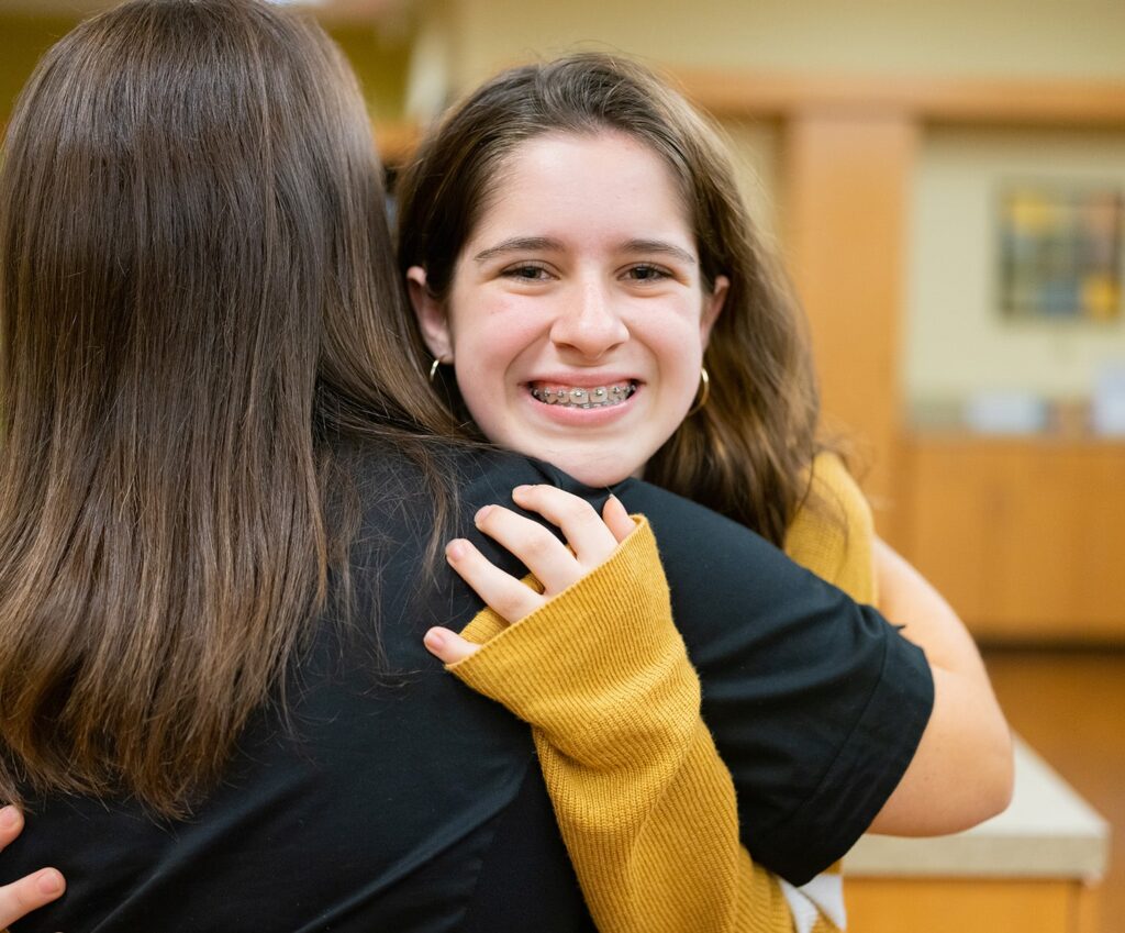 Close up of a smiling teen with braces hugging a Vinson Orthodontics treatment tech