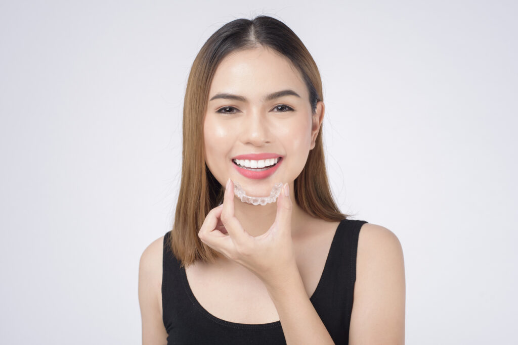 Portrait of a woman holding her Invisalign® aligner in front of her face while smiling